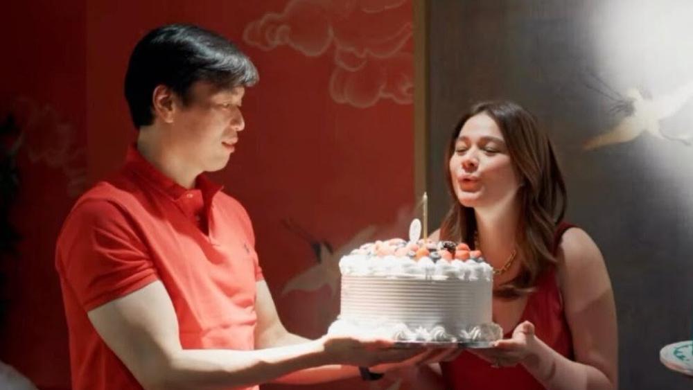赤い服のベア・アロンソが夫ヴィンセントに支えられた誕生日ケーキのろうそくを吹き消す