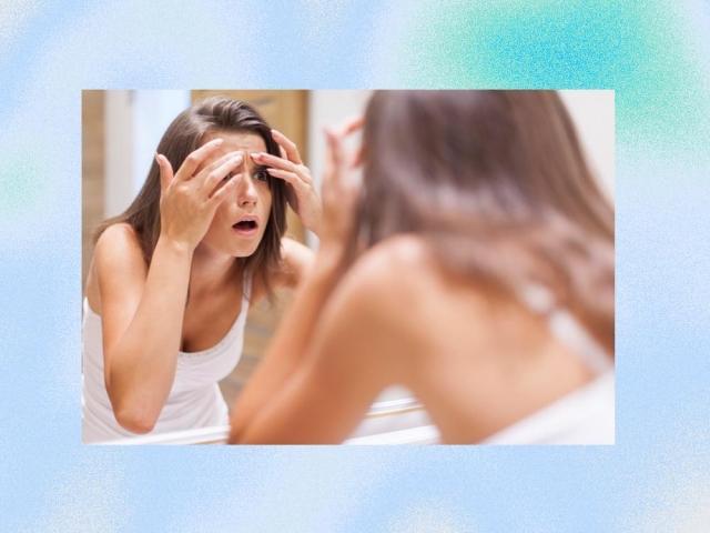 Shocked woman squeezing pimple in bathroom