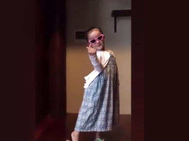 Zia Dantes wearing shades and a dress while giving a fingerheart